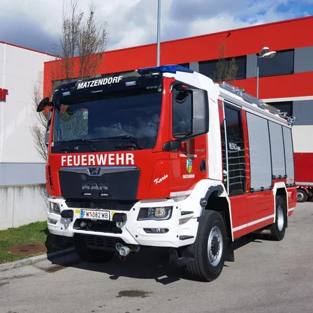 Ein roter und weißer Feuerwehrwagen steht vor einem roten Gebäude mit dem Wort 'MATZENDORF' oben.