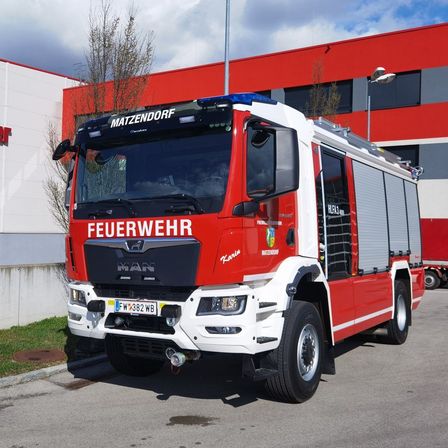 Ein roter und weißer Feuerwehrwagen steht vor einem roten Gebäude mit dem Wort 'MATZENDORF' oben.