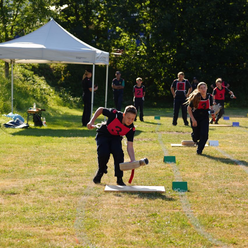 Eine Gruppe von Menschen spielt Cricket auf einem Rasenfeld. Eine Person hält einen Cricketschläger und scheint bereit zu sein, den Ball zu schlagen.