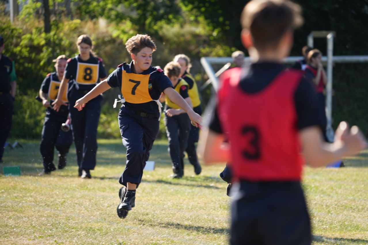 Ein Junge mit einem gelben Trikot mit der Nummer 7 läuft auf einem Grasfeld, möglicherweise an einem Schulsportevent teilnehmend.
