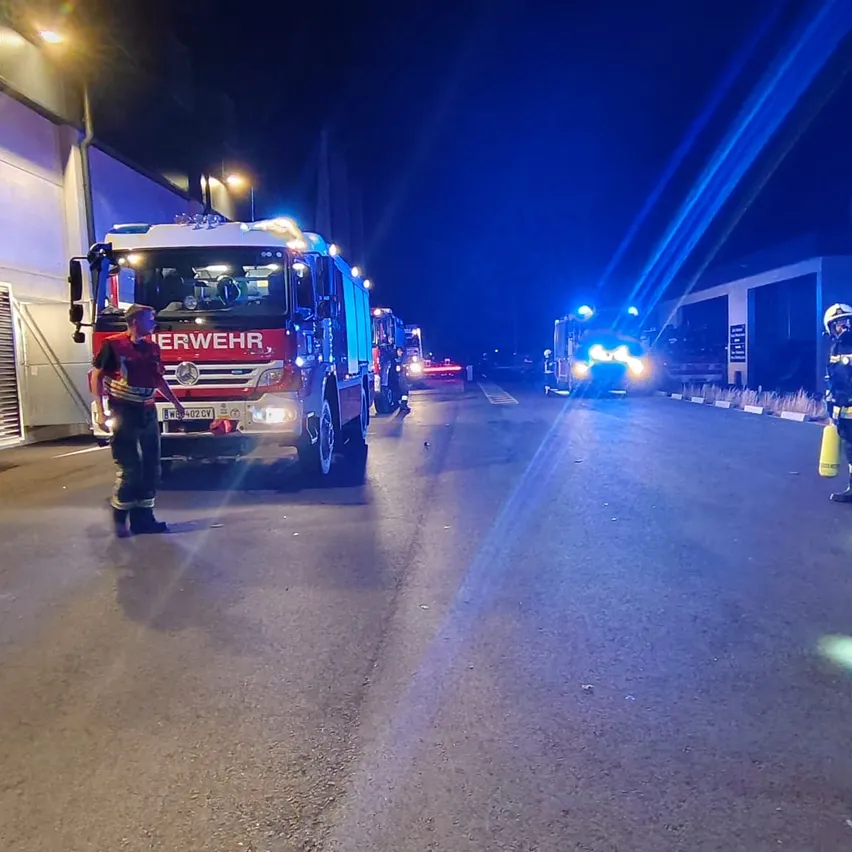 Feuerwehrleute stehen neben einem Feuerwehrauto mit blinkenden Lichtern auf einer Straße bei Nacht.