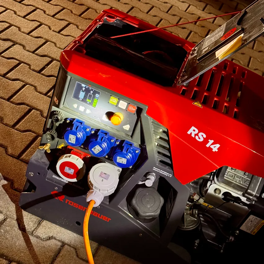 Ein roter und schwarzer Generator mit mehreren Steckern und einem angeschlossenen gelben Kabel, gekennzeichnet mit RS 14. Das Bedienfeld hat verschiedene Knöpfe und ein digitales Display.