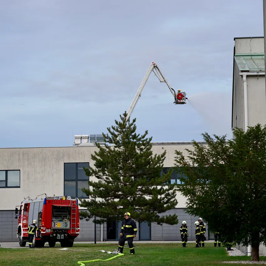Feuerwehrleute benutzen eine Leiter, um das Dach eines Gebäudes zu erreichen, während ein anderer Feuerwehrmann Wasser von einer Plattform sprüht.
