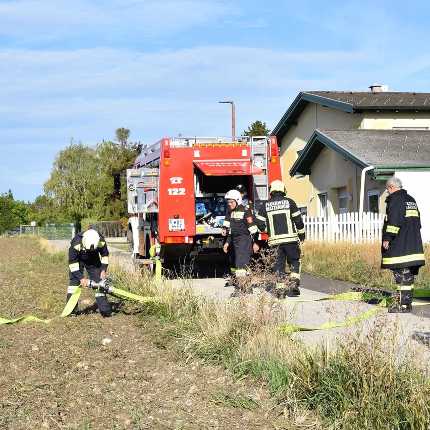 Feuerwehrleute bereiten einen Feuerwehrwagen vor einem Haus mit einer weißen Umzäunung vor. Ein Feuerwehrmann befestigt einen Schlauch am Wagen.