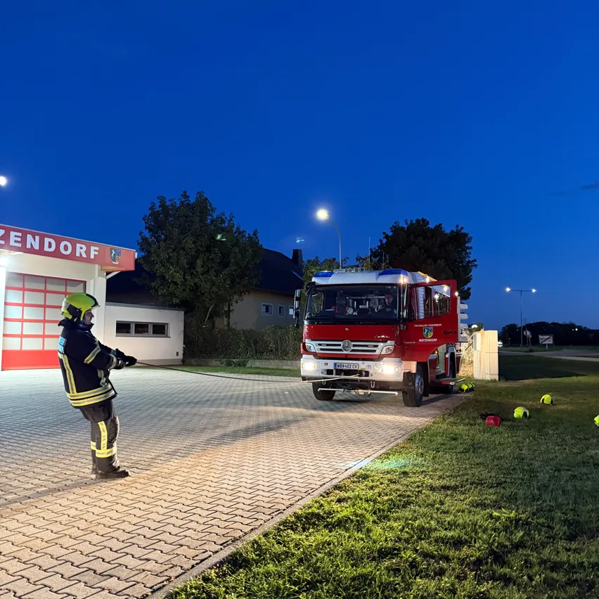 Ein Feuerwehrmann übt das Benutzen einer Feuerwehrschläuche vor einem Feuerwehrhaus bei Nacht.