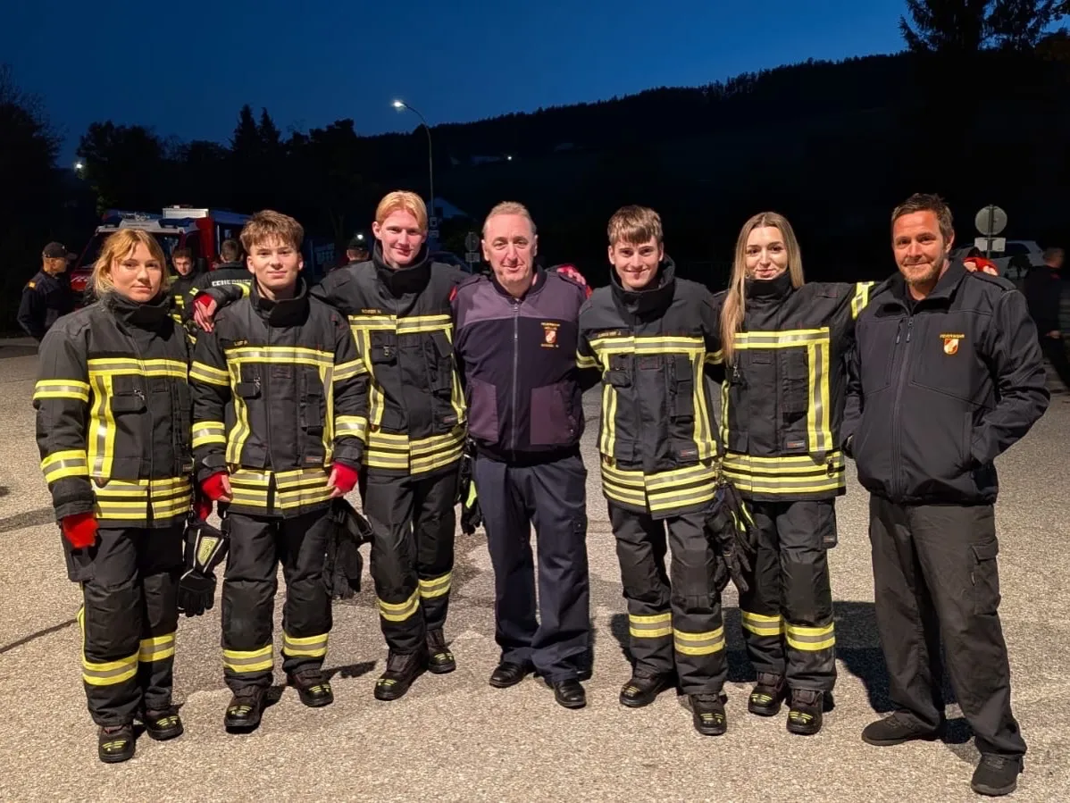 Eine Gruppe von Feuerwehrleuten, darunter zwei Frauen, stehen nachts zusammen auf einem Parkplatz.