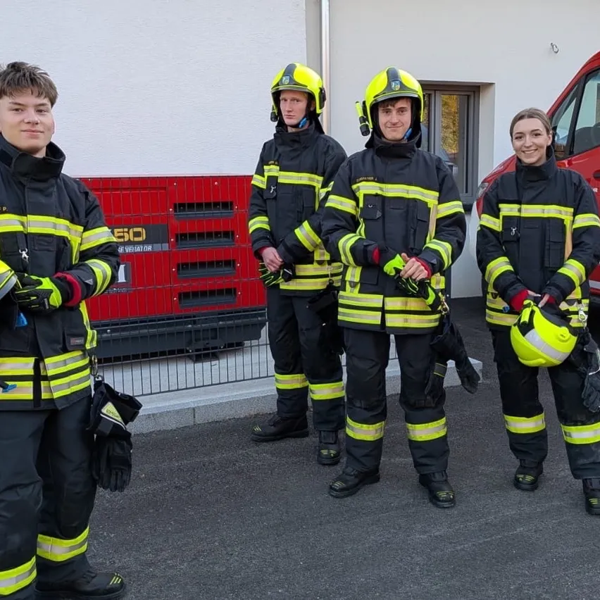 Fünf Feuerwehrleute in voller Uniform stehen zusammen vor einem Feuerwehrauto.