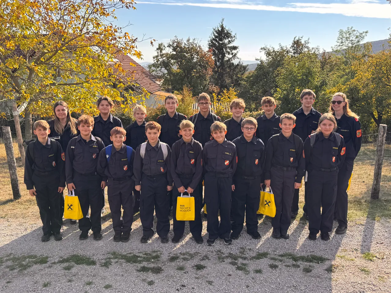 Eine Gruppe junger Menschen in Uniform posiert für ein Foto vor einem baumbestandenen Bereich.