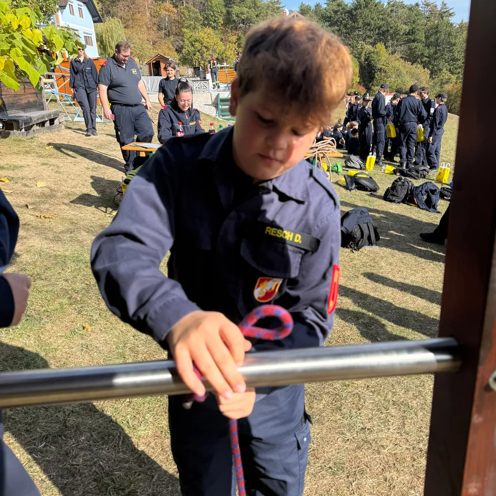 Ein Junge in einer dunkelblauen Uniform mit einem gelben Aufnäher auf der Schulter hält einen roten Seil, möglicherweise an einer Trainingsübung teilnehmend.