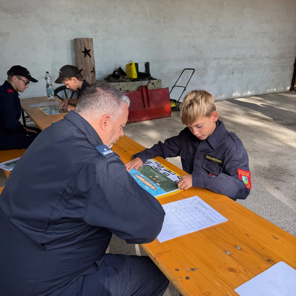 Ein Mann in Uniform sitzt mit einem Jungen in Uniform an einem Tisch und sie betrachten beide ein Puzzle auf dem Tisch.