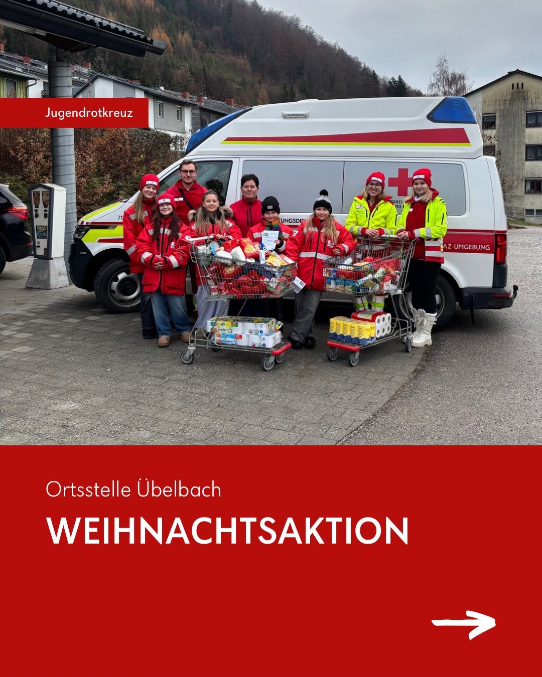 Eine Gruppe von Freiwilligen posiert vor einem Krankenwagen mit Spenden in Einkaufswagen. Das Bild trägt den Titel 'Ortsstelle Ubelbach Weihnachtsaktion.'