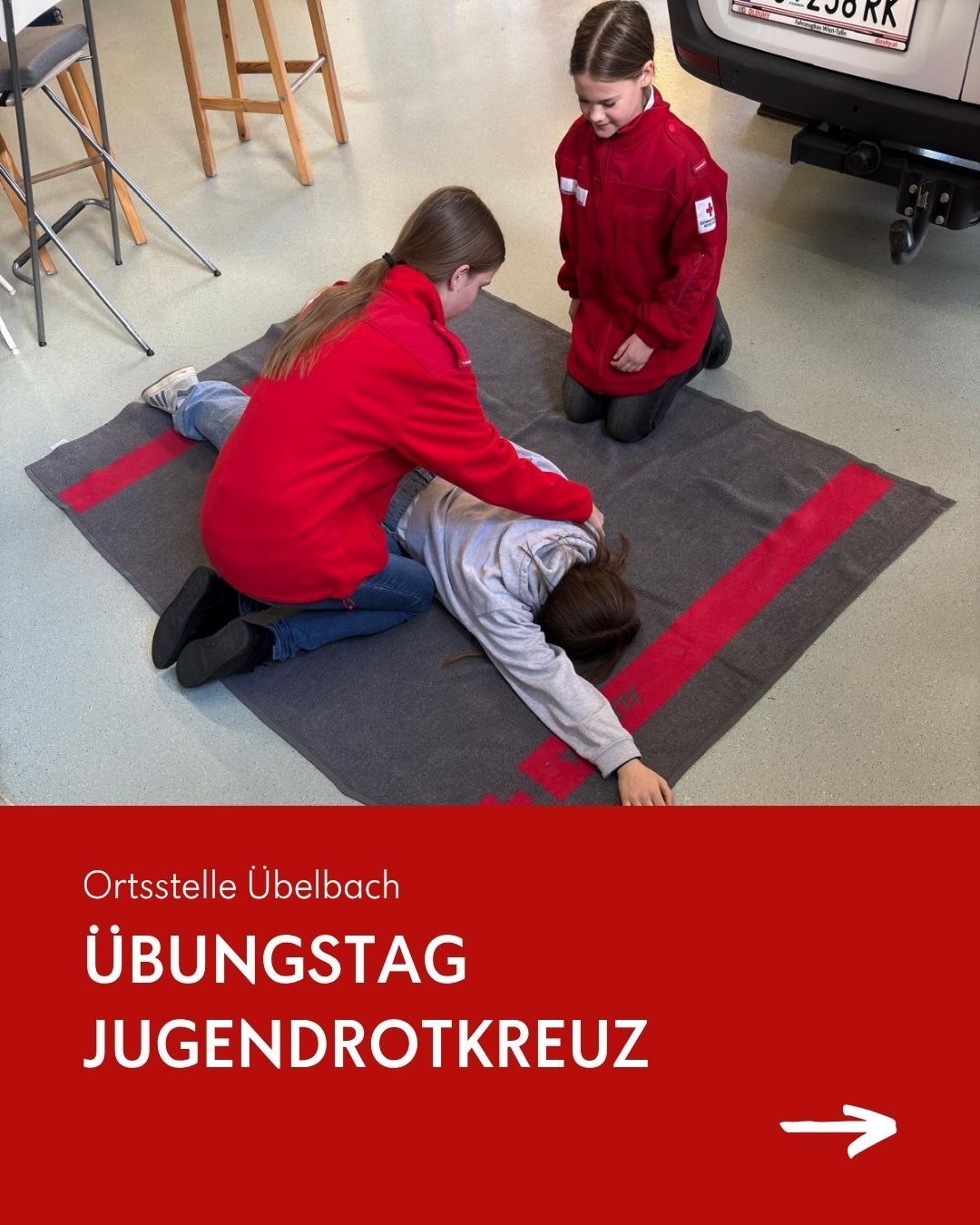Ein Übungstag an der Ortsstelle Ubelbach des Jugendrotkreuz. Zwei Personen in roten Jacken leisten Erste Hilfe einer Person, die auf einem grauen Teppich mit roten Linien liegt. Unten befindet sich ein roter Banner mit weißem Text.