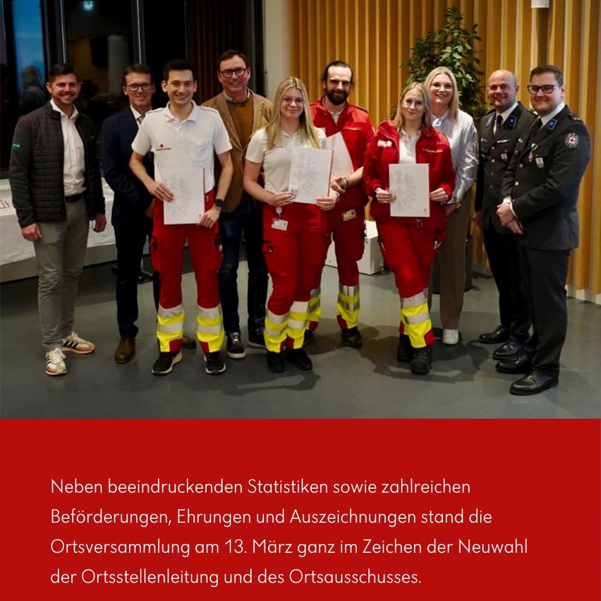 Eine Gruppe von Menschen, darunter sowohl Männer als auch Frauen, steht vor einer gelben Wand. Sie tragen rote Uniformen und halten Urkunden in den Händen. Sie scheinen ein besonderes Ereignis zu feiern.