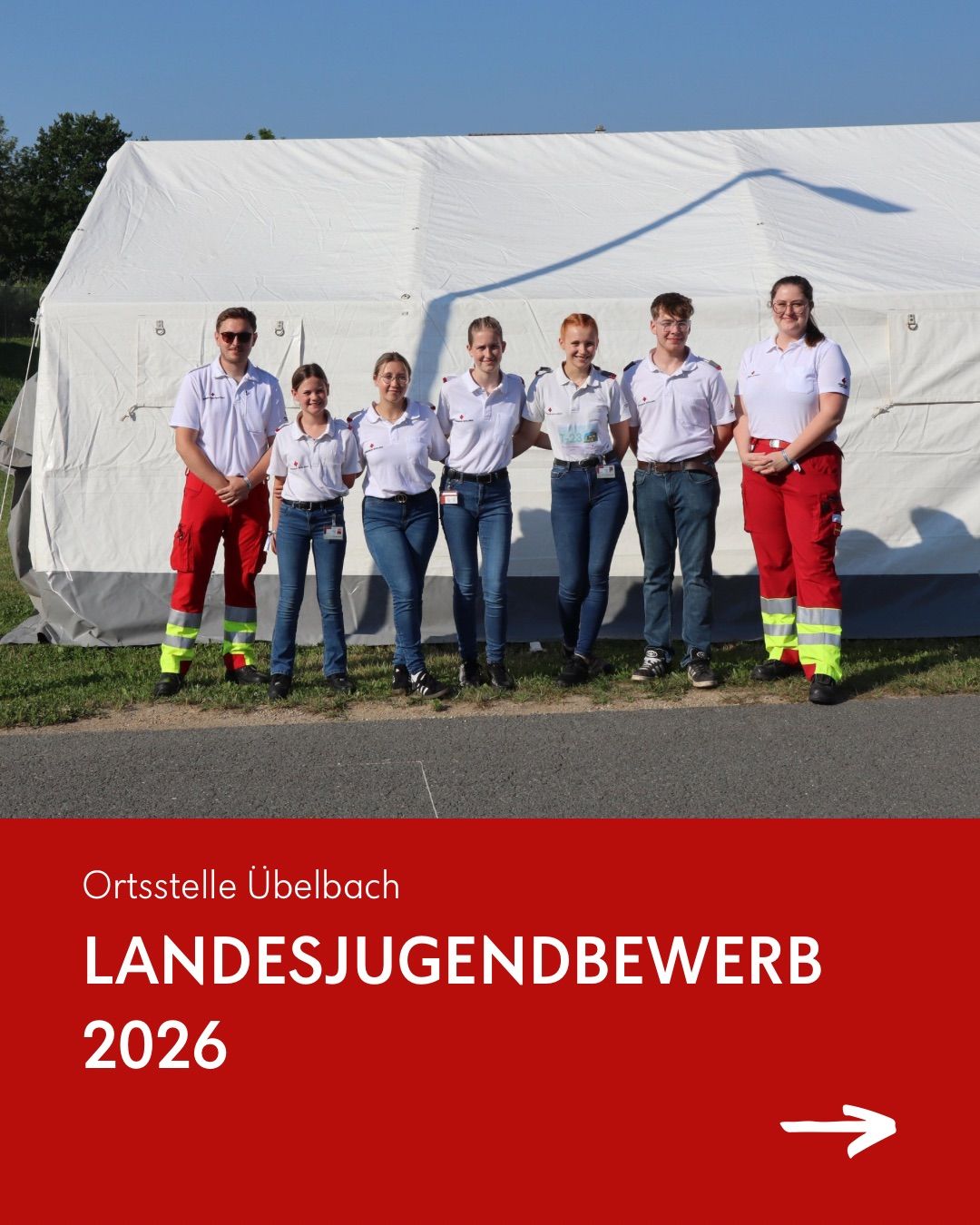 Sechs Personen in Uniformen stehen vor einem weißen Zelt, das mit Ortsstelle Ubelbach beschriftet ist. Sie lächeln und scheinen für ein Foto zu posieren. Das Bild hat einen roten Rand.