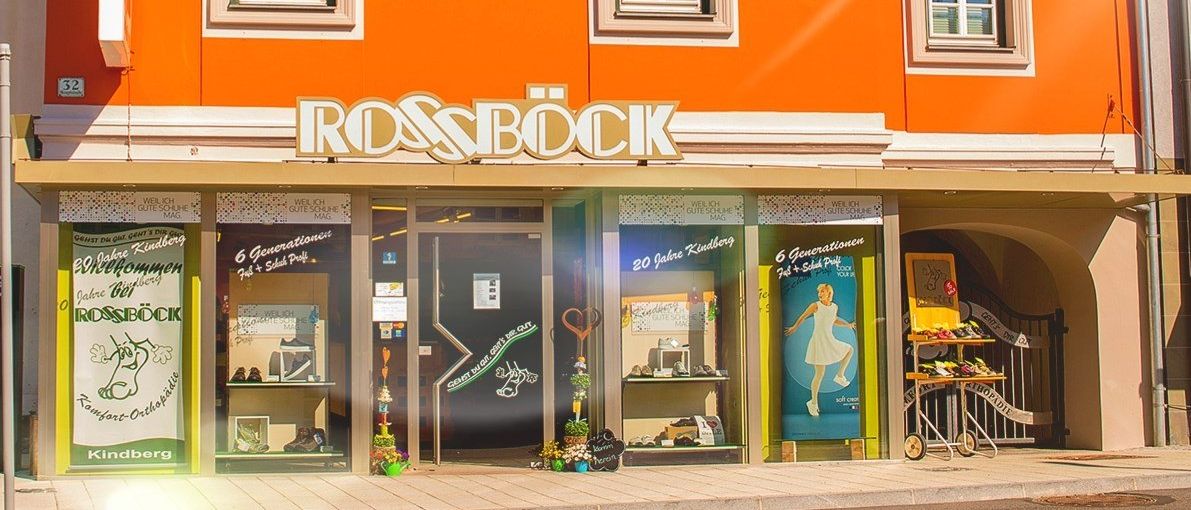 Ein leuchtend oranges Gebäude namens Rossbock an einem sonnigen Tag. Es hat weiße Verkleidungen und drei Fenster im zweiten Stock und drei im ersten.