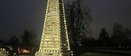 Ein hoher Holzstapel mit einem Weihnachtsbaum auf der Spitze ist bei Nacht in einem offenen Feld beleuchtet.