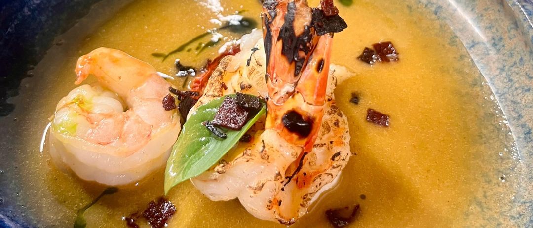 Eine Schüssel Suppe mit Garnelen, garniert mit Blättern und roten Chilischoten auf einem Tisch mit anderen Schüsseln.