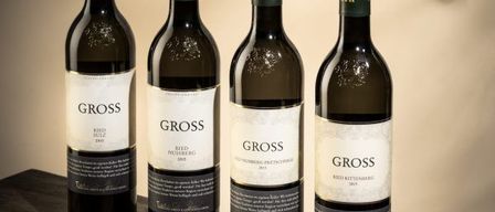 Four bottles of Gross wine, with varying labels and vintages, are displayed on a wooden table.