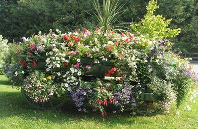 Ein mit bunten Blumen gefüllter Wagen steht auf dem Gras. Im Hintergrund sind Bäume.