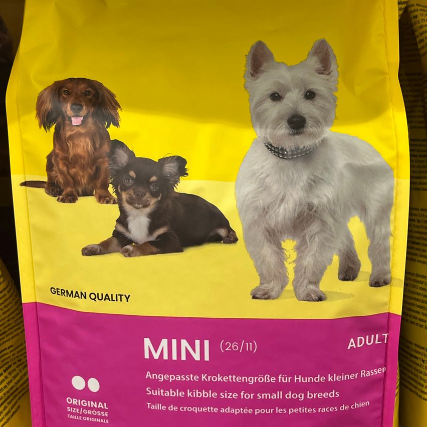 Eine Tüte Hundefutter namens MINI, geeignet für kleine Hunderassen. Es zeigt drei Hunde, einen braunen, einen schwarzen und einen weißen. Die Marke behauptet, es sei von deutscher Qualität.