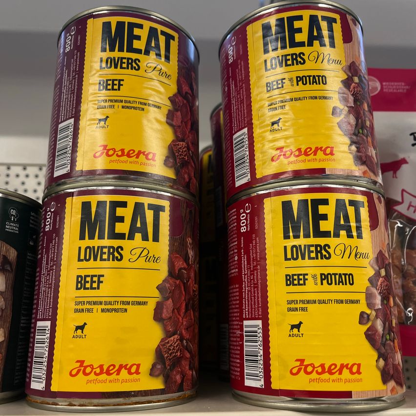 Mehrere Dosen Meat Lovers Pure und Meat Lovers Menu Rindfleisch-Haustierfutter von Josera gestapelt auf einem Regal.