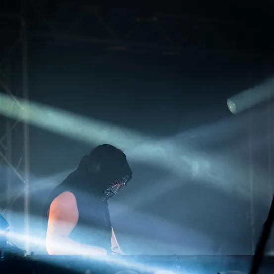 Ein maskierter Performer spielt auf der Bühne ein Keyboard, umgeben von blauem Licht und Rauch.