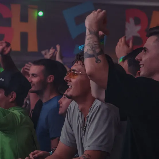 Eine Menschenmenge bei einem Musikfestival. Einige jubeln mit erhobenen Händen. Der Mann in der Mitte hat eine Tätowierung am Arm.
