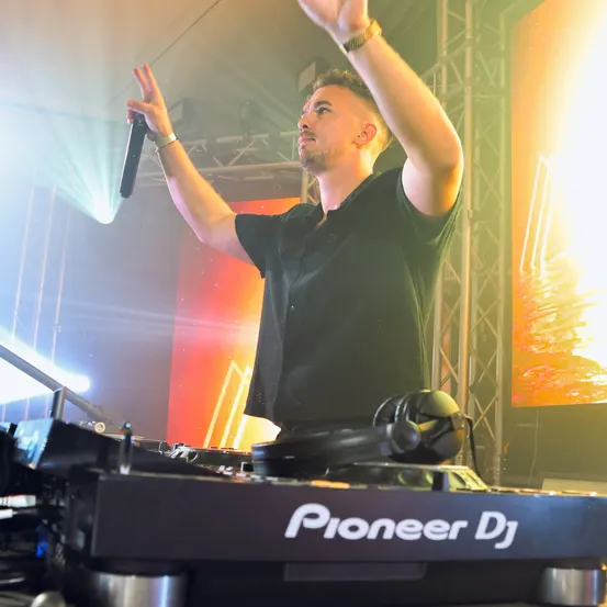 Ein Mann tritt auf der Bühne auf, hält ein Mikrofon und spielt an einem Pioneer DJ-Turntable.
