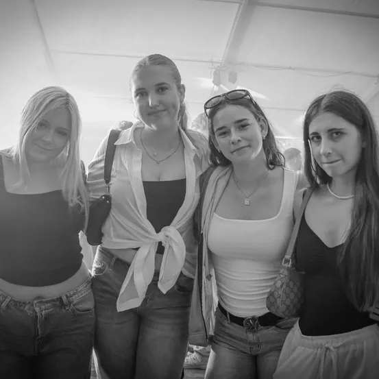 Vier Frauen posieren für ein Foto in einem überdachten Bereich, wahrscheinlich bei einer Veranstaltung. Sie tragen Freizeitkleidung, eine von ihnen hat eine Sonnenbrille auf dem Kopf.