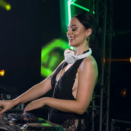 Eine DJ-Frau lächelt und spielt auf einem DJ-Mixer bei einer Musikveranstaltung unter grünem Licht.