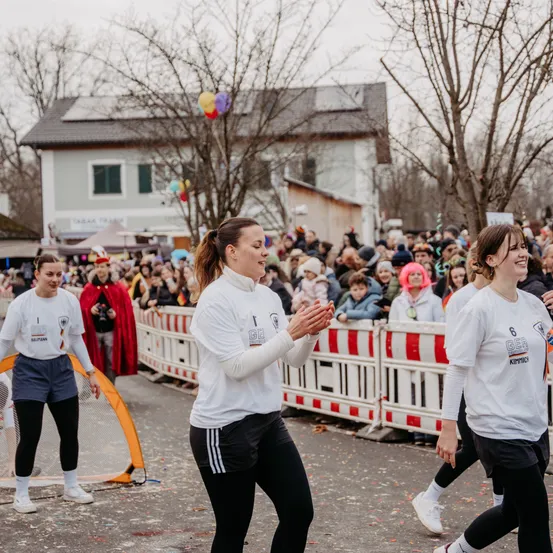 Drei Frauen gehen vor einer jubelnden Menge. Sie tragen weiße Trikots und schwarze Hosen. Hinter ihnen steht eine Menge Menschen und schaut zu. Im Hintergrund ist ein Haus zu sehen.