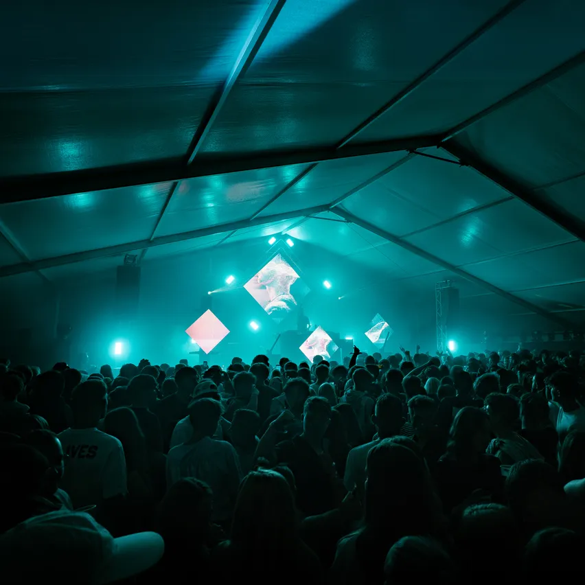 Eine große Menschenmenge versammelt sich in einem Zelt für ein Konzert unter blauem Licht.