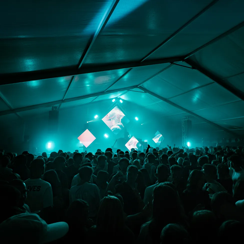 Eine große Menschenmenge versammelt sich in einem Zelt für ein Konzert unter blauem Licht.