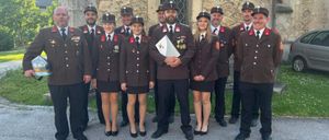 Eine Gruppe uniformierter Personen, bestehend aus Männern und Frauen, steht vor einem Gebäude aus Stein. Sie tragen Hüte und Schuhe.
