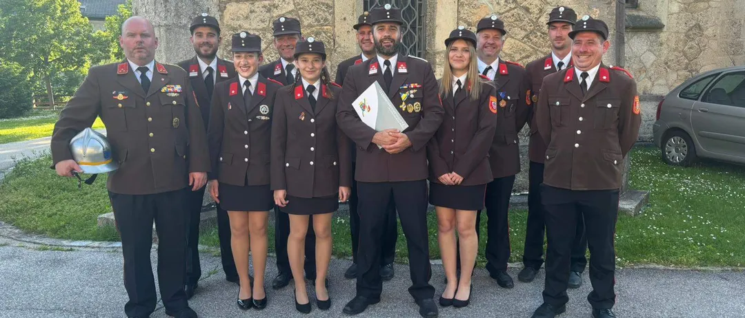 Eine Gruppe uniformierter Personen, bestehend aus Männern und Frauen, steht vor einem Gebäude aus Stein. Sie tragen Hüte und Schuhe.