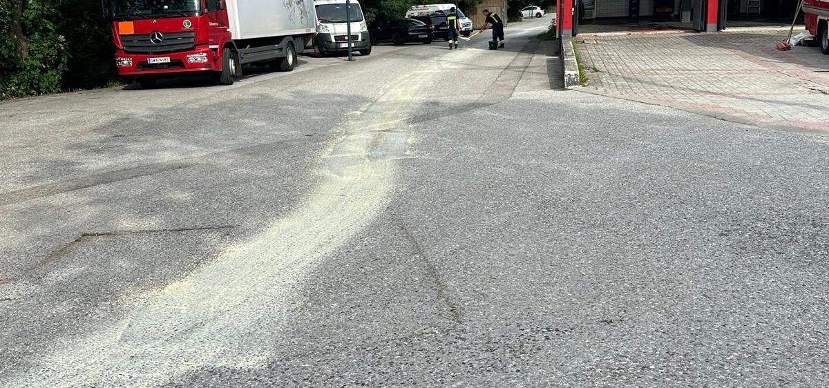 Ein roter und weißer Lkw ist am Straßenrand geparkt, in der Nähe einer Feuerwache. Bäume und geparkte Autos sind im Hintergrund.