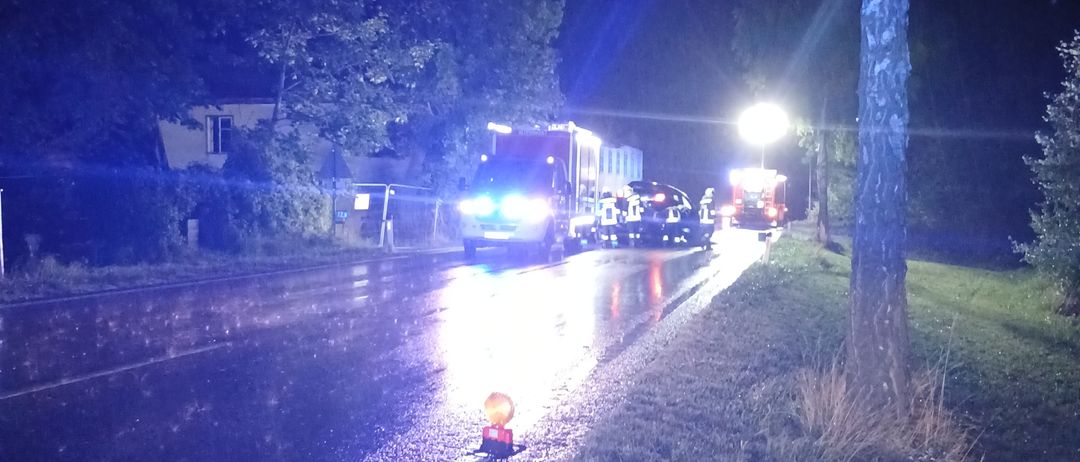 Notfallfahrzeuge stehen bei Nacht auf einer nassen Straße, ihre Lichter sind eingeschaltet und ein Gebäude ist im Hintergrund sichtbar.