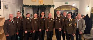 Eine Gruppe von Männern in Militäruniformen steht in einem Raum mit gefliesten Böden. Sie posieren für ein Foto mit einer festlichen Girlande im Hintergrund.