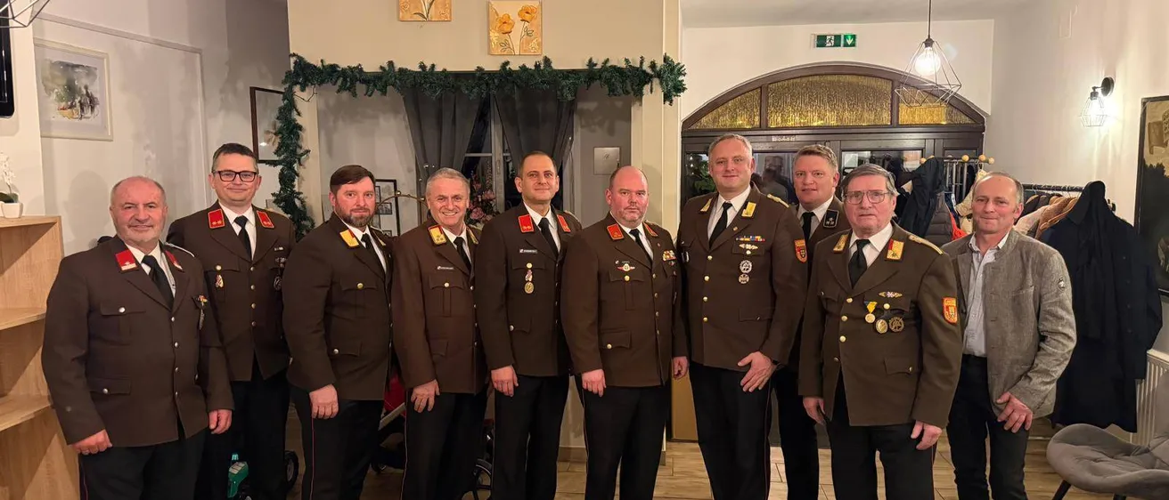 Eine Gruppe von Männern in Militäruniformen steht in einem Raum mit gefliesten Böden. Sie posieren für ein Foto mit einer festlichen Girlande im Hintergrund.