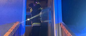 Ein Feuerwehrmann steht nachts in einem Haus, hält eine Taschenlampe in der Hand und schaut auf ein Glasfenster.