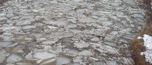 Ein gefrorener Fluss mit zerbrochenen Eisstücken und etwas Schnee an den Seiten.