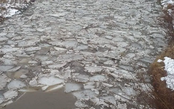 Ein gefrorener Fluss mit zerbrochenen Eisstücken und etwas Schnee an den Seiten.