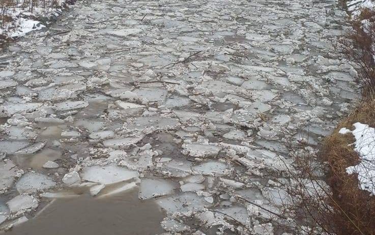 Ein gefrorener Fluss mit zerbrochenen Eisstücken und etwas Schnee an den Seiten.