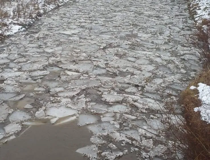 Ein gefrorener Fluss mit zerbrochenen Eisstücken und etwas Schnee an den Seiten.