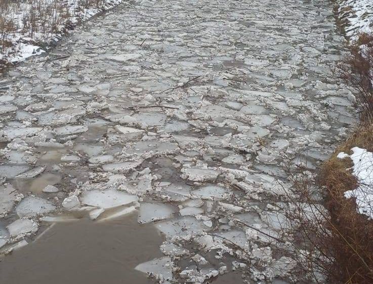 Ein gefrorener Fluss mit zerbrochenen Eisstücken und etwas Schnee an den Seiten.
