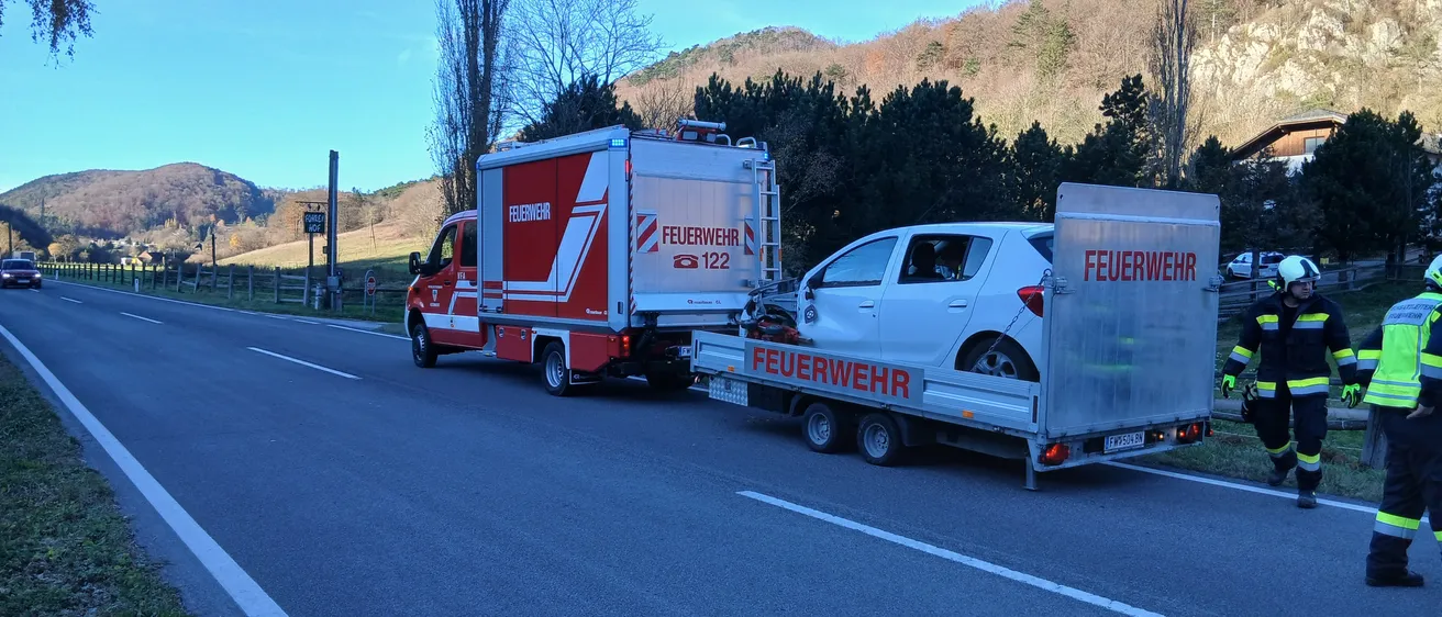 Ein Feuerwehrfahrzeug zieht ein Auto an der Straßenseite, wobei eine Person in einer reflektierenden Weste steht.