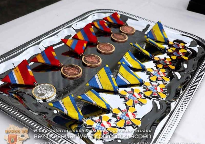 Ein silbernes Tablett zeigt mehrere Medaillen, einschließlich roter, gelber und blauer Bänder mit goldenen Zentren. Die Medaillen sind in einer Reihe angeordnet und reflektieren die Oberfläche des Tabletts.