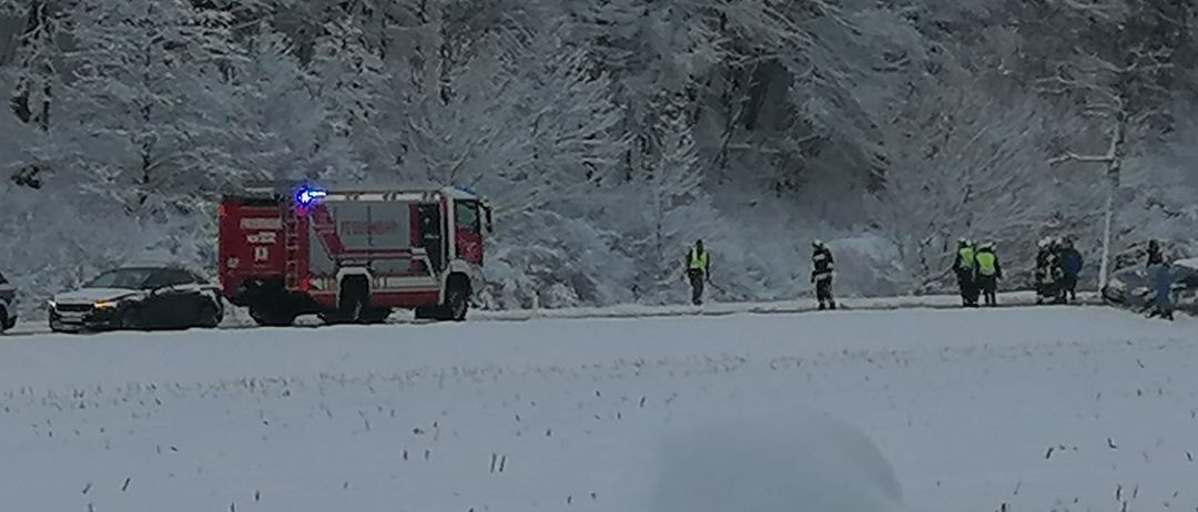 Ein Feuerwehrauto steht in einem verschneiten Gebiet, wo zwei Personen auf dem Schnee gehen. Das Fahrzeug ist mit einer Leiter an der Seite ausgestattet.