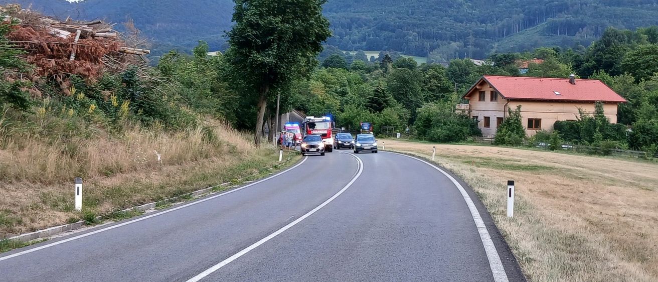 Einsatzfahrzeuge sind am Straßenrand geparkt, mit einem Haus und Bergen im Hintergrund.