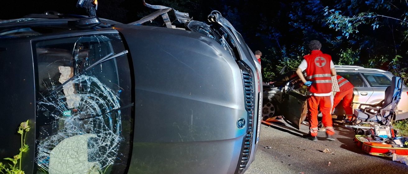 Ein Auto liegt nachts auf der Seite auf der Straße, Rettungskräfte sind am Unfallort.